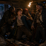 Young boy surrounded by rough pirates in a dim log cabin lit by a torch, a parrot perched on a pirate's shoulder nearby.