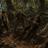 Group of men in period clothing battling in a muddy forest trench among trees.