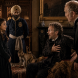 Young girl in a black dress speaks with two men in a richly decorated room; a blue-clad servant and a dog nearby.